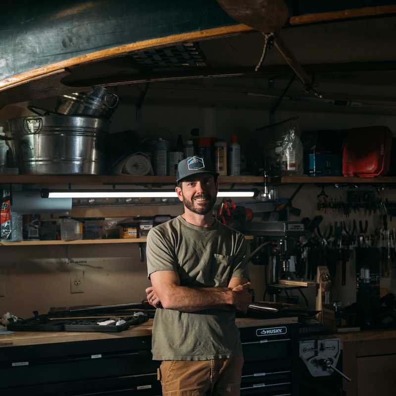 A bartender in a hat stands behind the bar inside a Montana saloon, with shelves of bottles and bar tools in the background