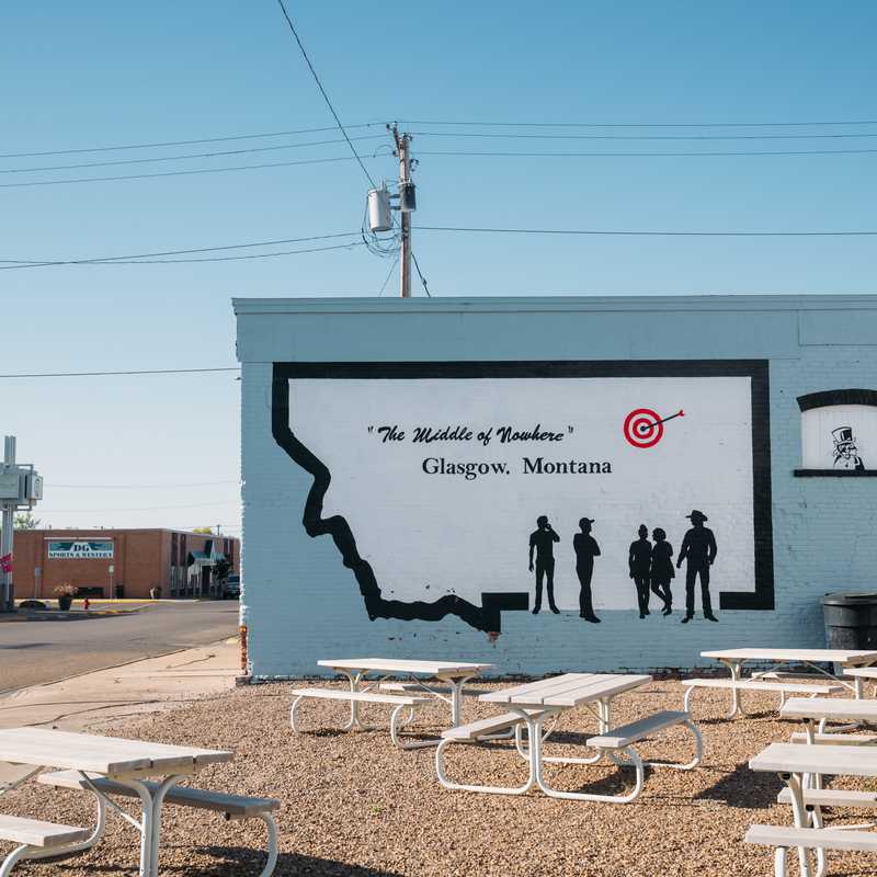 Outdoor mural on a building in Glasgow, Montana featuring the outline of Montana and silhouettes of people with a “The Mighty H’s” slogan