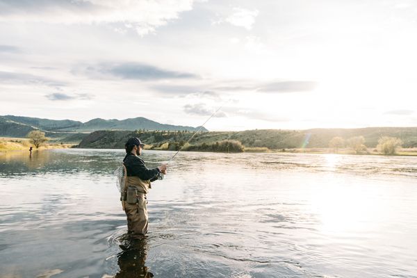 Person standing in a calm Montana lake at sunset with rolling hills and mountains in the distance