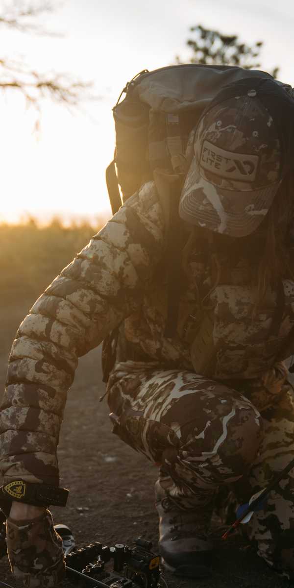 Person in camouflage sitting in a vehicle outdoors at sunrise with hands on a control handle