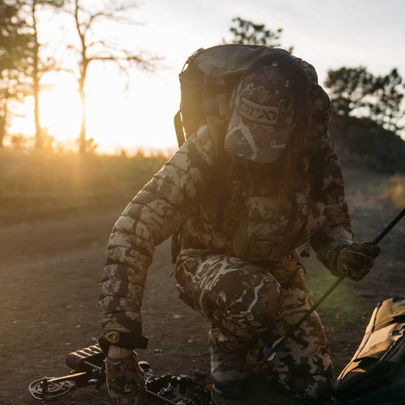 Person in camouflage sitting in a vehicle outdoors at sunrise with hands on a control handle
