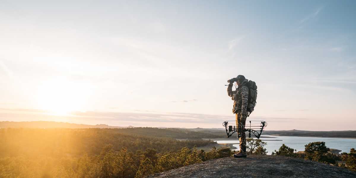 Backpacker with a large pack standing on a rocky overlook above a lake at sunrise in Montana