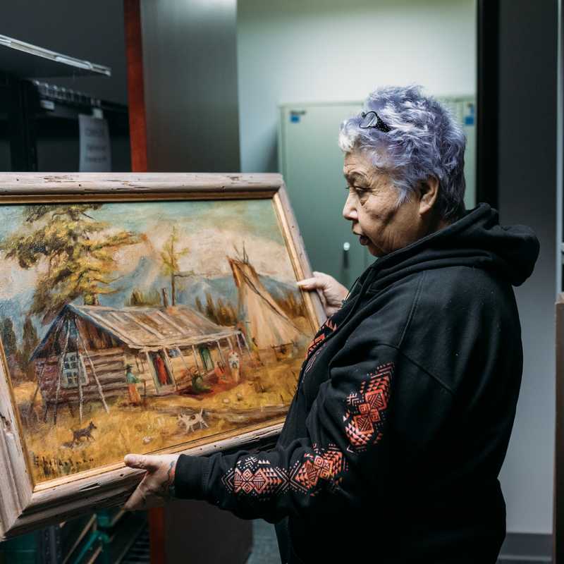 Person holding a framed landscape painting inside an art storage or gallery space