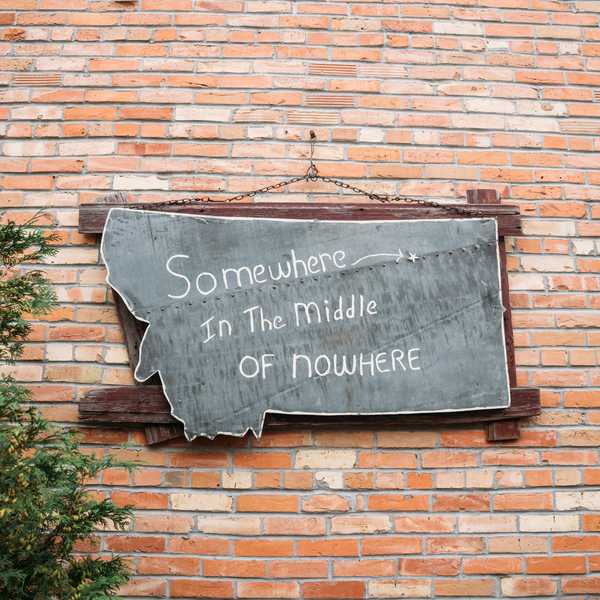 Metal Montana-shaped sign on a brick wall reading “Somewhere in the Middle of Nowhere”