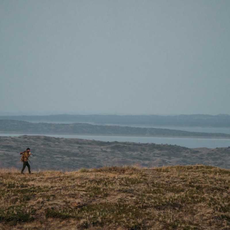 Hiker walking along a coastal bluff overlooking waves and distant shoreline in Montana
