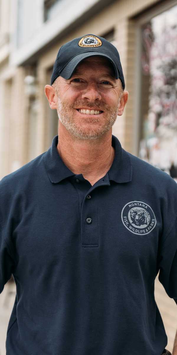 Man wearing a Montana cap and polo shirt standing on a city sidewalk near storefronts
