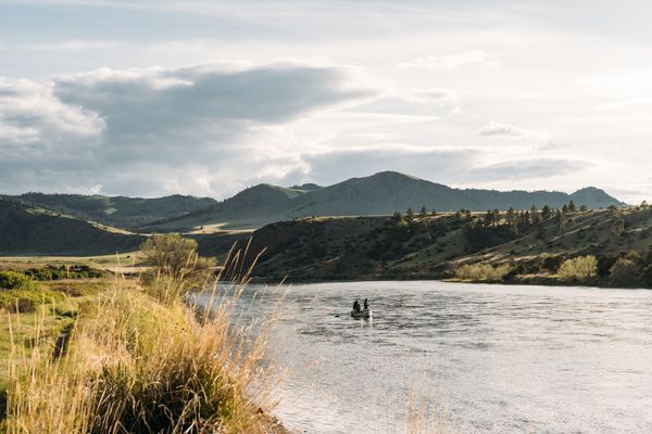 People kayaking on a Montana river with forested hills and mountains in the background