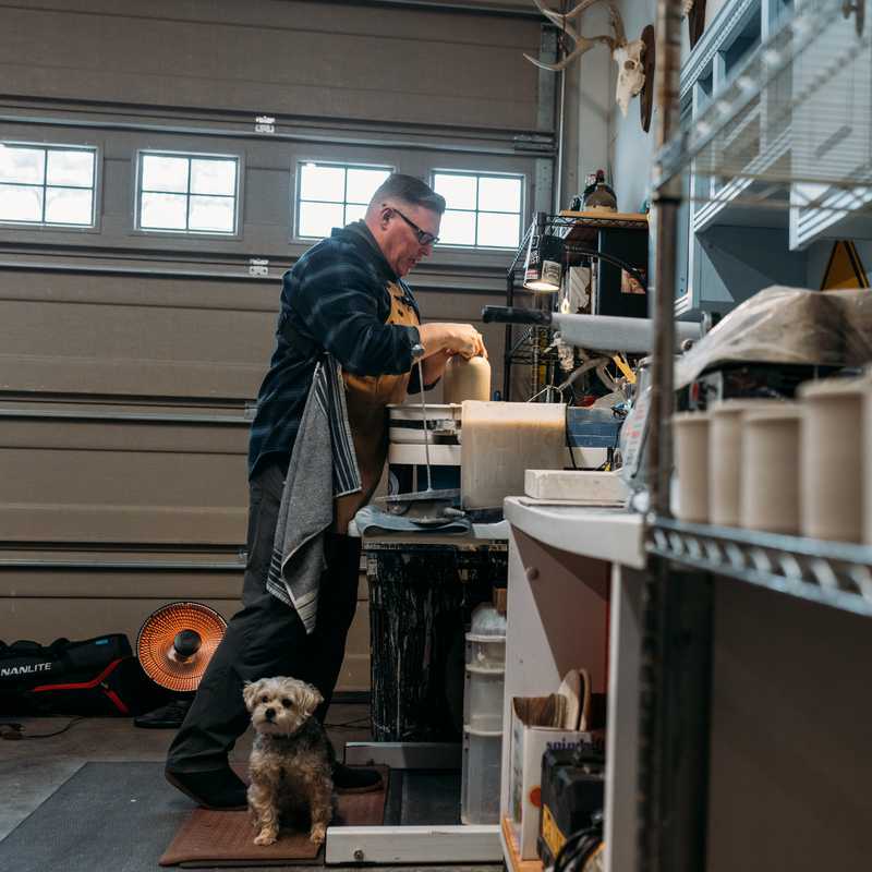 Person working in a workshop next to shelves and tools, with a dog nearby on the floor