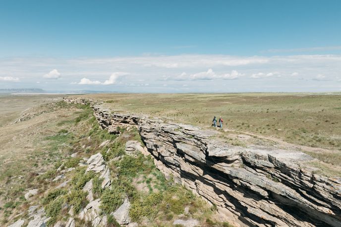 Hikers walk along a rocky ridge on a vast Montana prairie under a wide sky