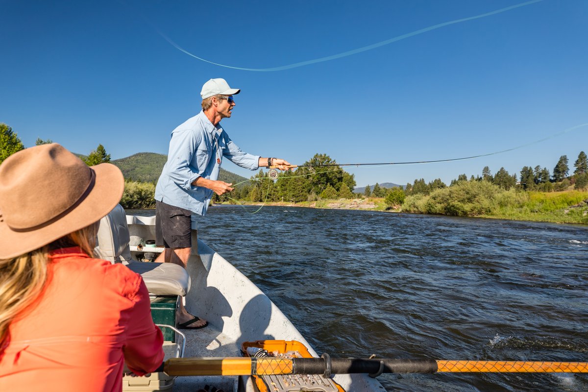 Two people on a small boat fishing on a Montana river under a blue sky
