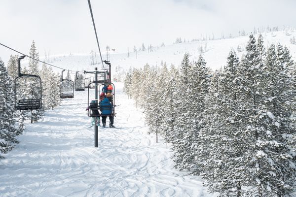 Ski lift traveling over snow-covered trees in a Montana mountain landscape with distant riders and chair cables