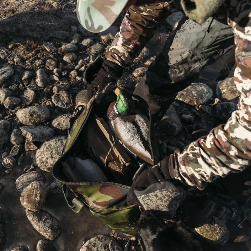 Person crouching on a rocky riverbank with a fishing line and tackle near the water