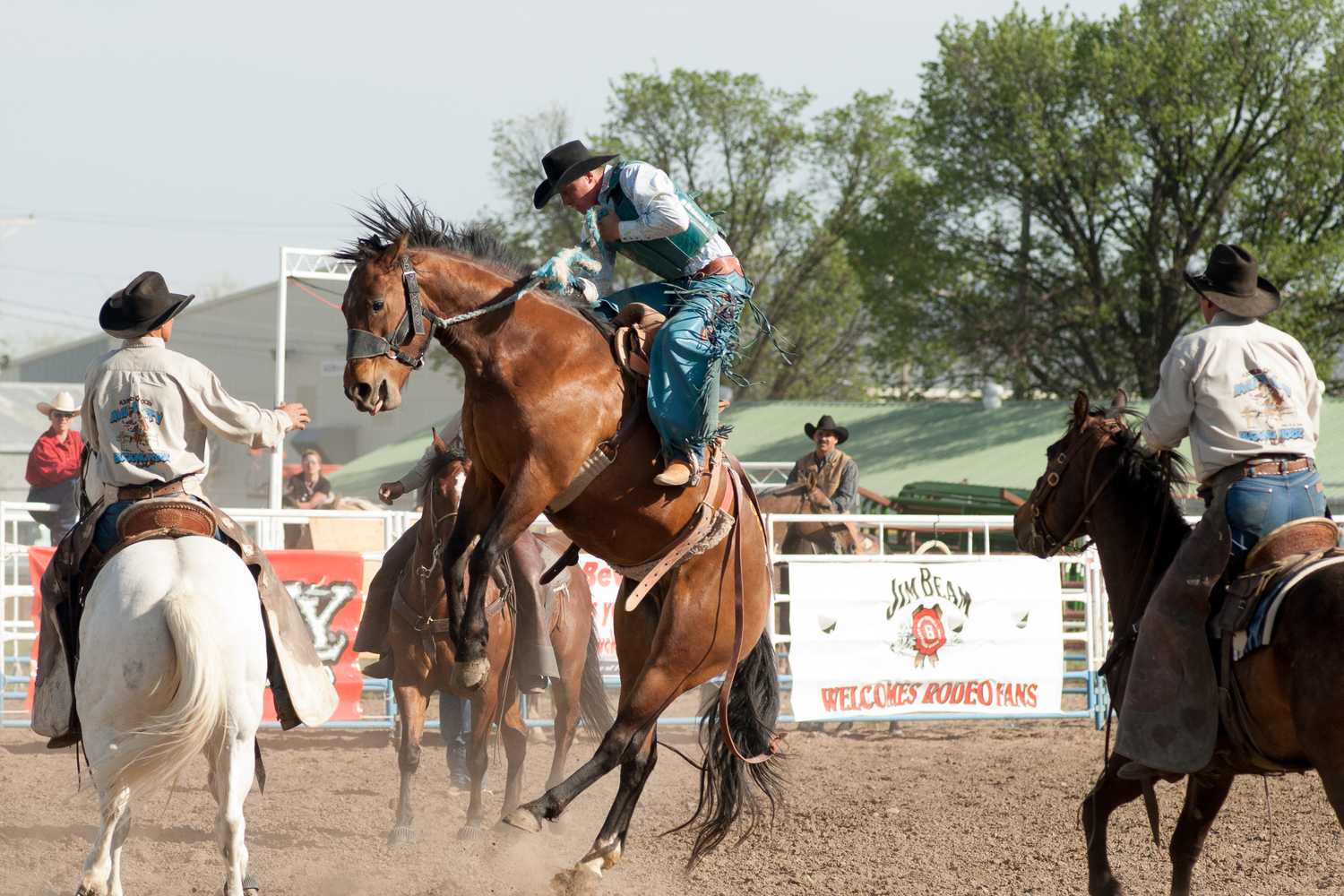 Horse race at a rodeo arena, with a rider on horseback in the center surrounded by other riders and horses near the track fence