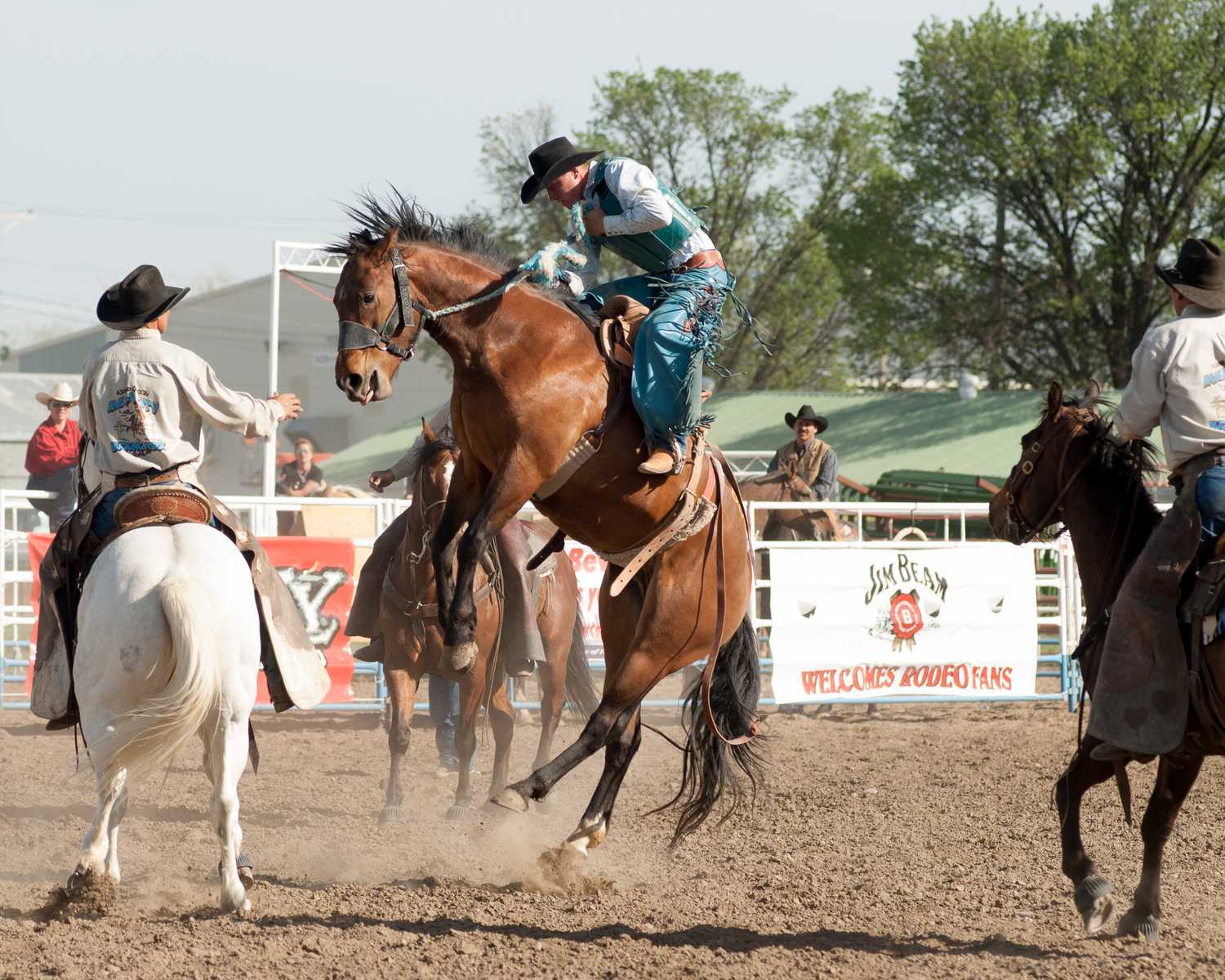 Horse race at a rodeo arena, with a rider on horseback in the center surrounded by other riders and horses near the track fence