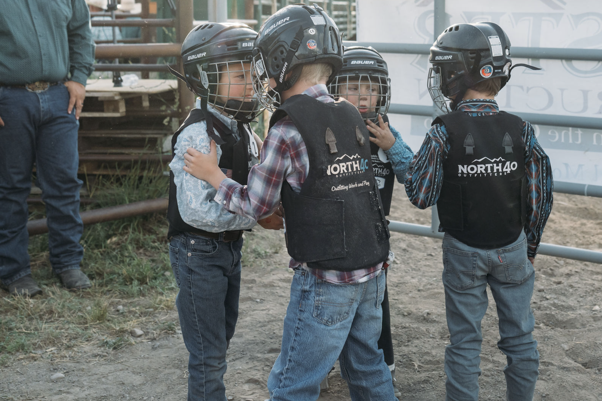 Children wearing racing helmets and protective vests stand near a race vehicle at a North40 event in Montana