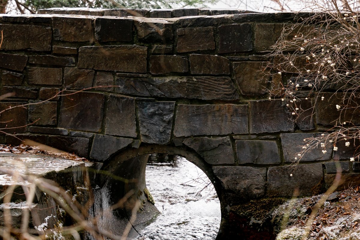 Stone arch bridge over a small creek in a wooded Montana setting in winter