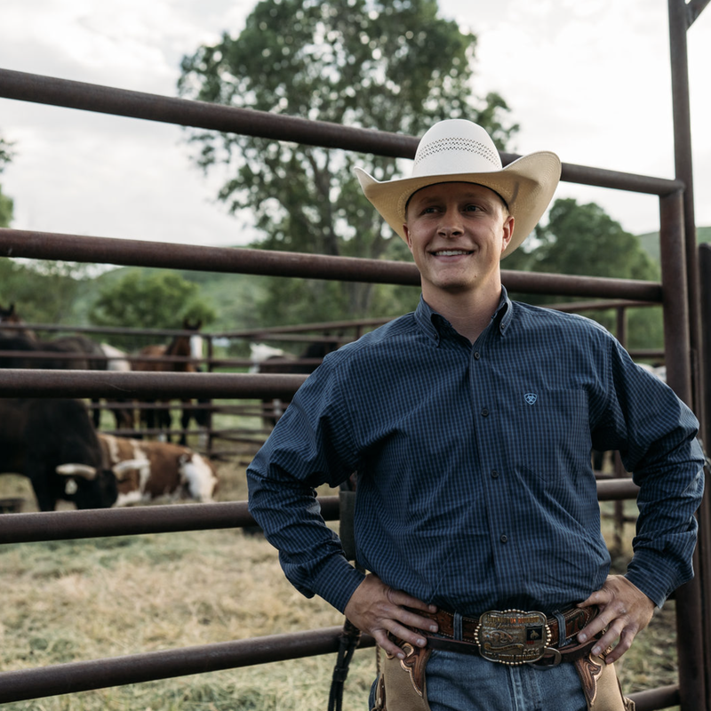 Cattle ranch worker wearing a white cowboy hat standing in a fenced pasture with cattle behind him in Montana