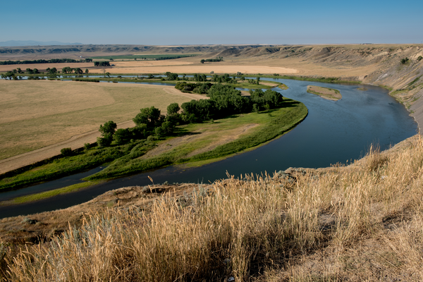 Meandering Yellowstone River flowing through grassy valley with farmland and rolling hills in Montana