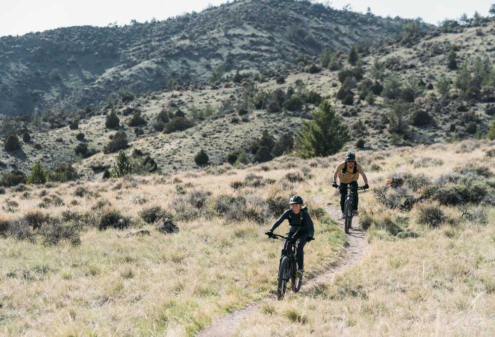 Cyclists ride a winding trail through dry grasslands and rocky hills in Montana