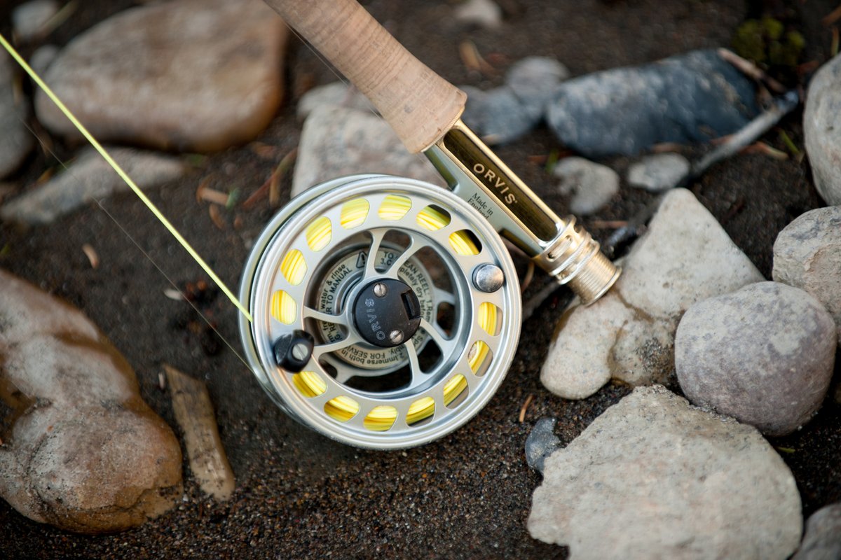 Fishing reel on a rocky riverbank with line cast nearby