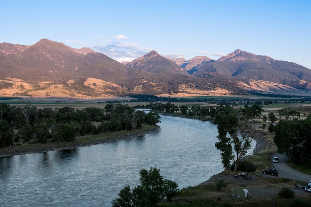 Wide view of the Yellowstone River flowing through Montana with mountains in the background and a riverside park along the shoreline