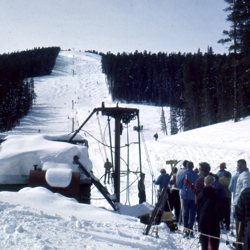 People line up near snowmaking equipment on a snowy Montana ski slope