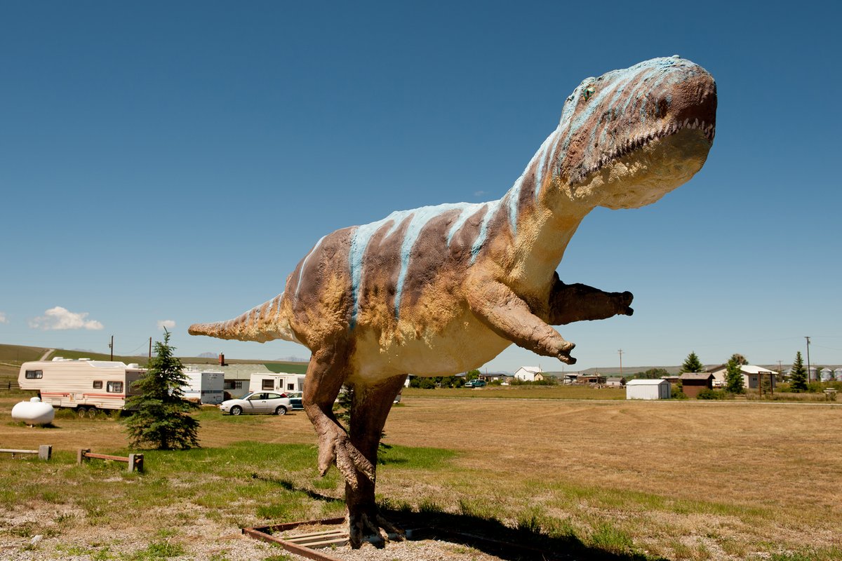 Life-size dinosaur statue standing in a grassy area with an RV campground in the background