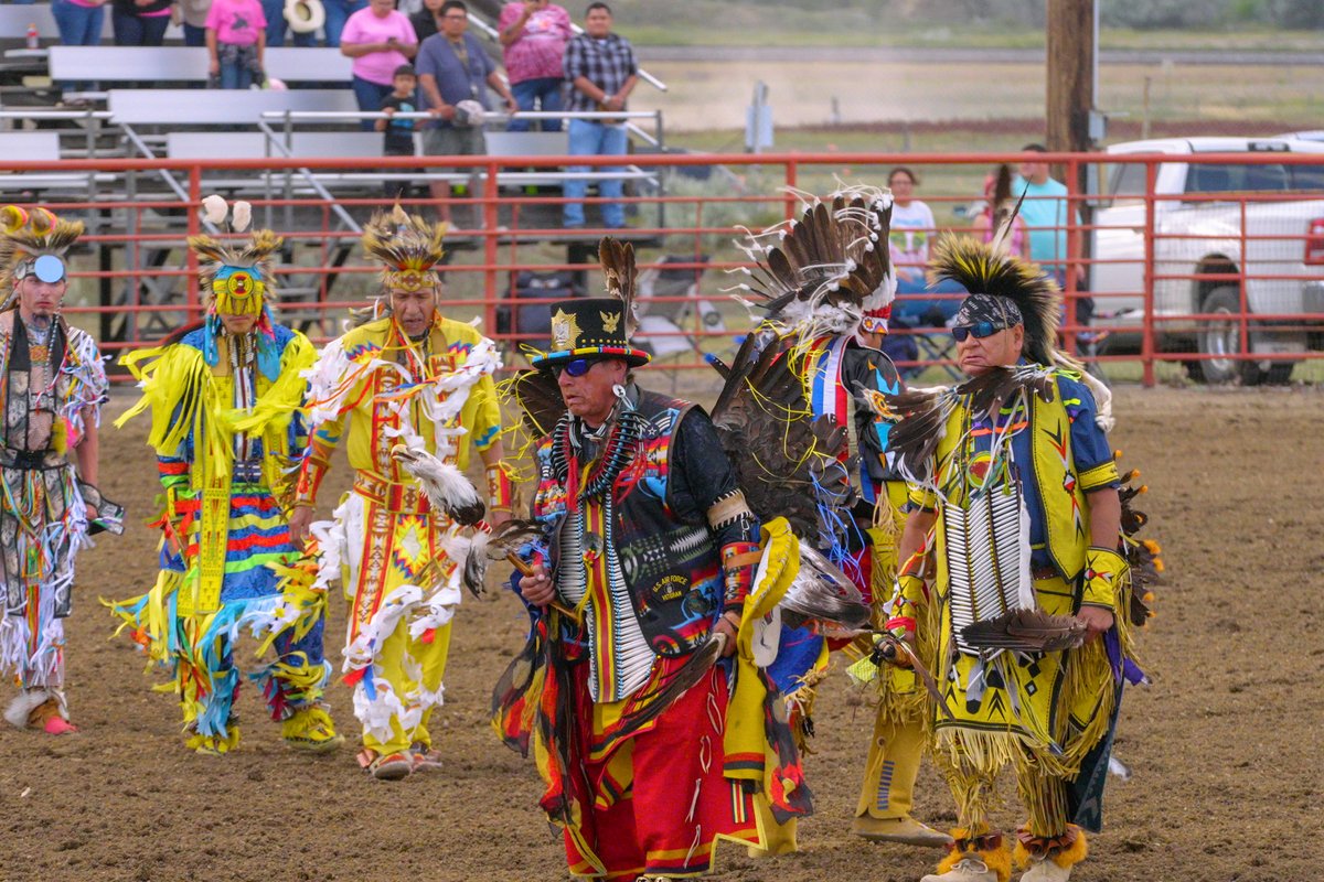 Crow dancers in colorful regalia moving forward at a rodeo arena in Montana