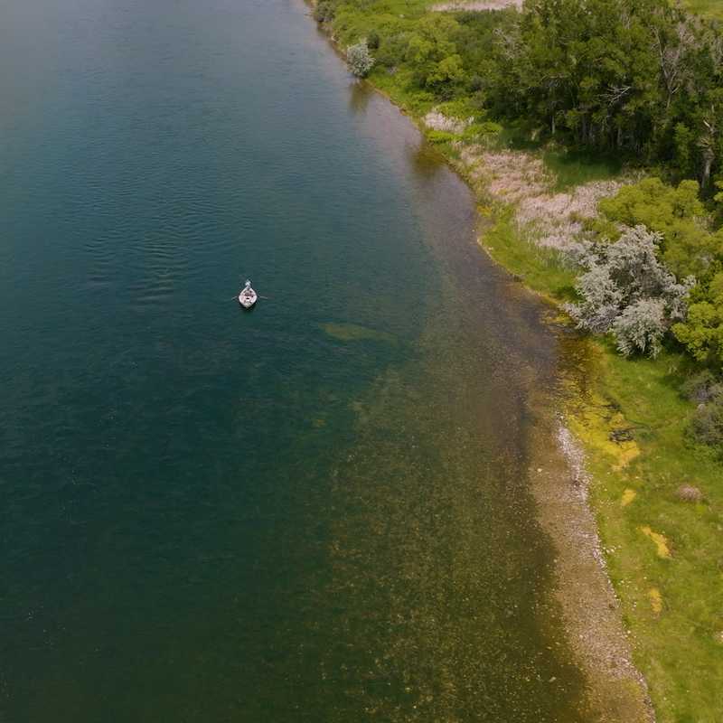 A river with small boats and a green shoreline lined with trees in Montana