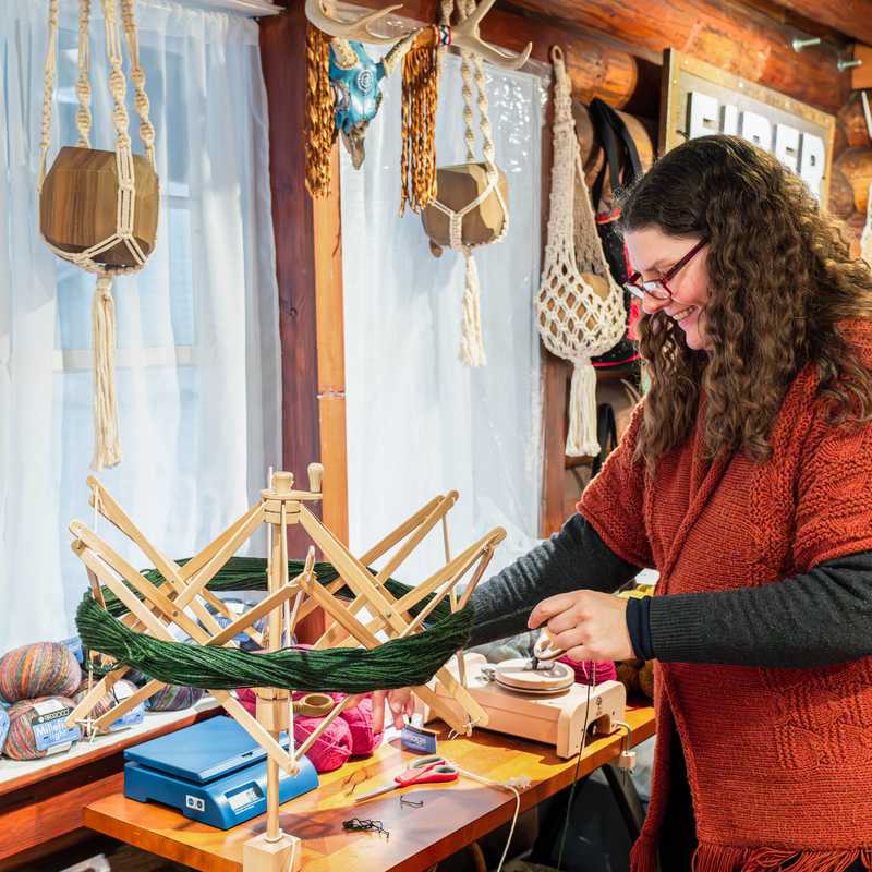 Woman working at a craft table inside a Montana cabin, making macramé-style items and assembling handmade decor pieces on wooden dowels