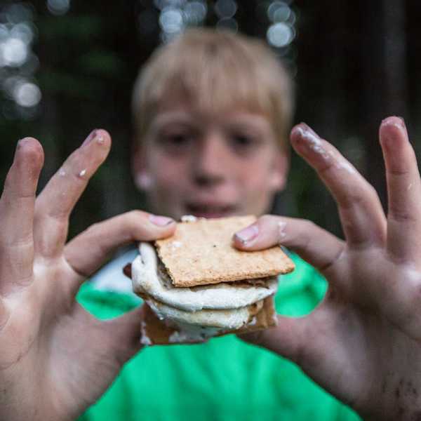 Child holding up a peanut-butter sandwich with both hands outdoors in Montana summer greenery
