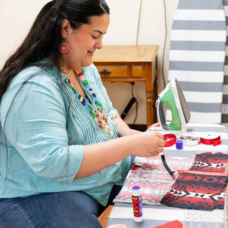 Woman sitting at a table working on a craft project with fabric and thread, using scissors and decorating supplies