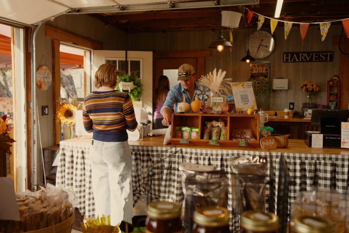 Farmers market vendor stall in Montana with breads, jars, and produce for sale under string lights