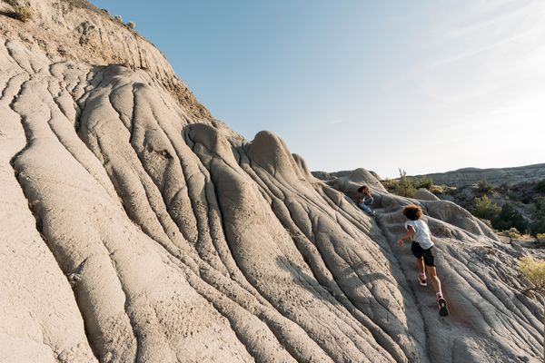 Hiker running along a pale, ridged rock formation at a Montana badlands landscape under a bright sky