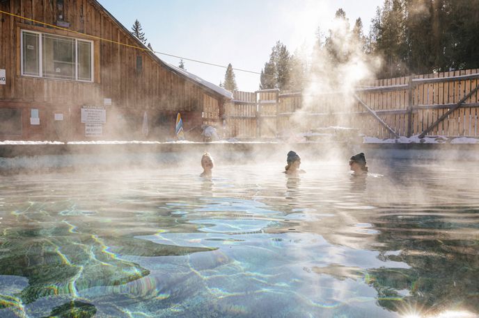 People soak in steaming geothermal hot springs near wooden buildings in Montana