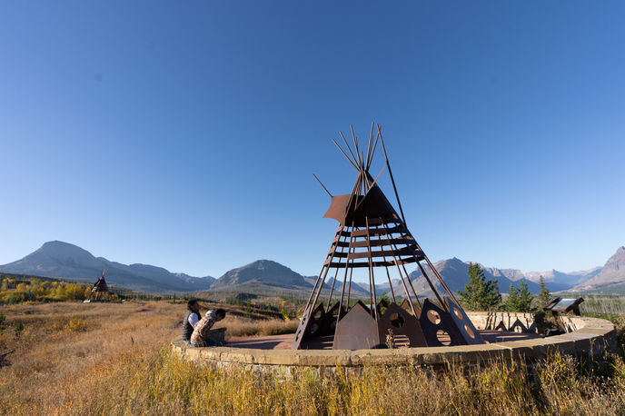 Historic tipi structure on the prairie with mountains and blue sky in the background