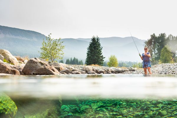 Person standing in a river on a calm day with distant mountains and trees in view