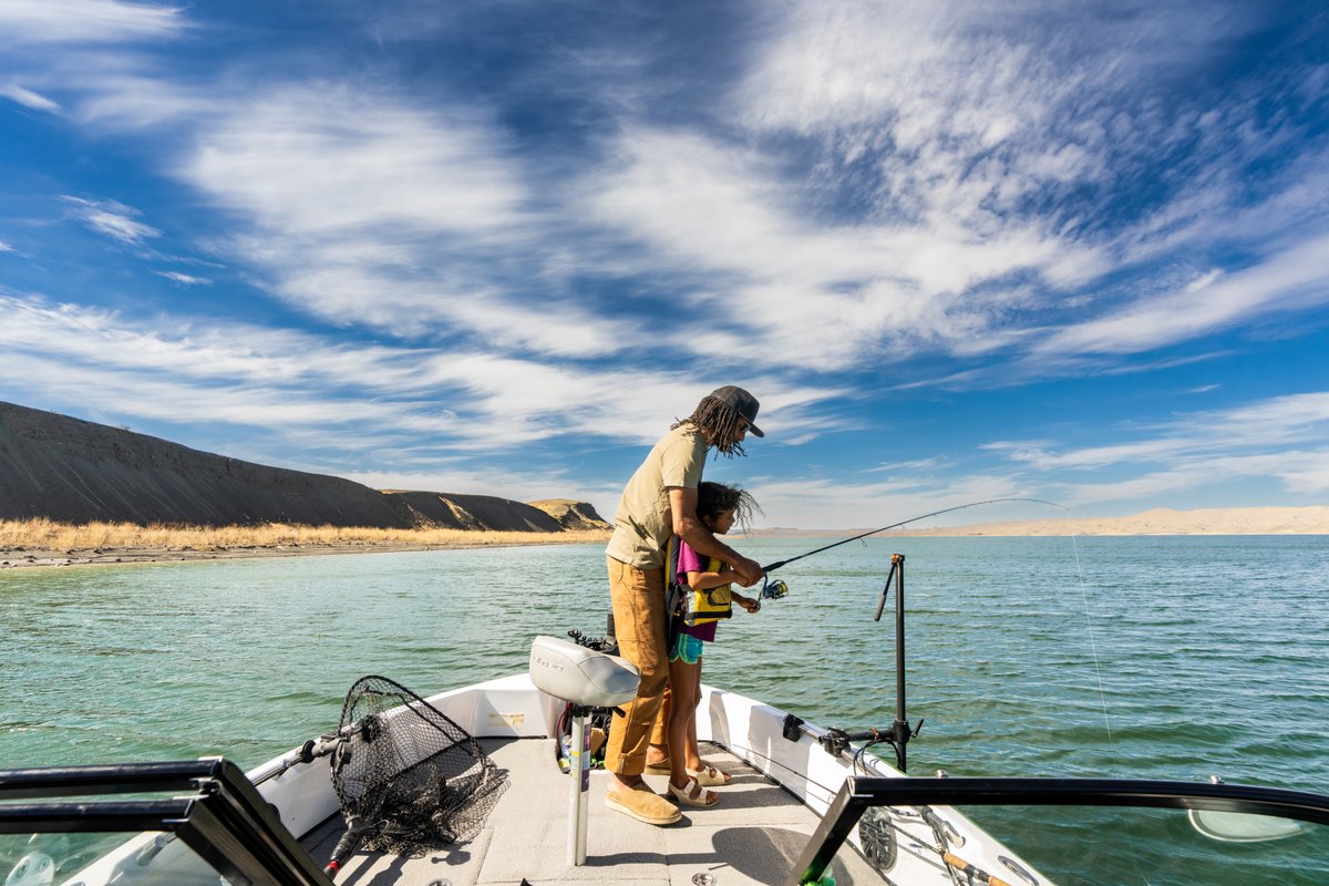 Woman fishing from a boat on a Montana lake under a blue sky with clouds