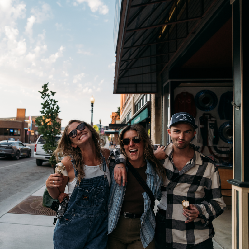 Friends walking on a downtown Montana sidewalk, smiling and holding drinks near storefronts