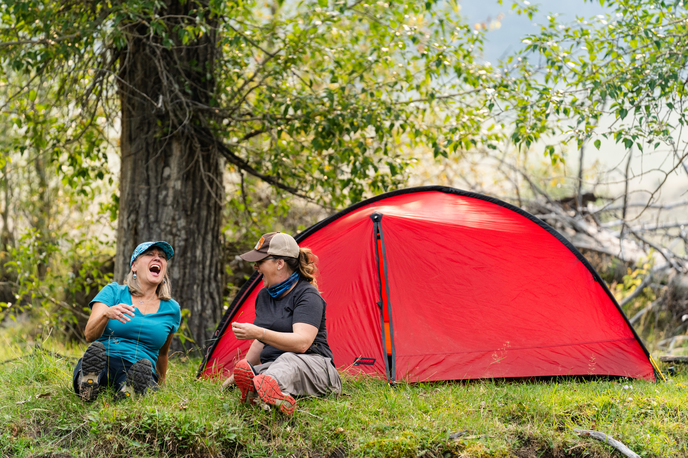 Campers relaxing beside a red tent in a Montana forest clearing