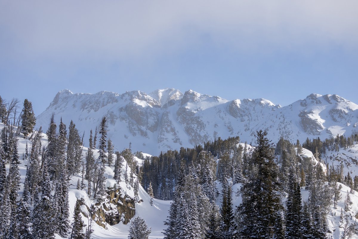 Snow-covered mountains and evergreen forests under a partly cloudy sky in Montana