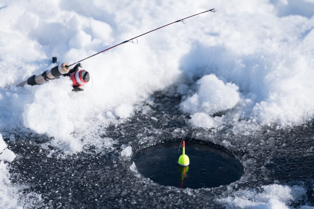 Angler fishing from a boat in choppy water during an ice-fishing competition, with a rod casting line into an open hole