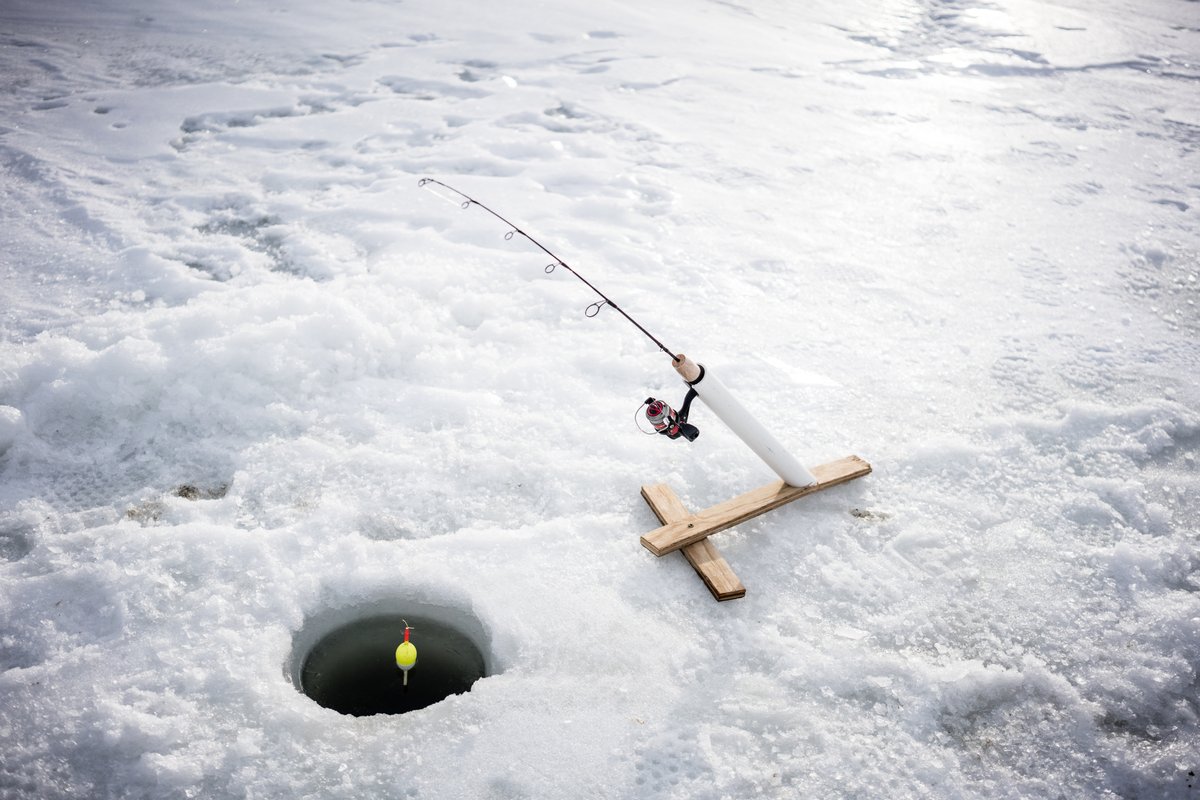 Snowkitersn on a small skisled propels across icy snow while ice fishing through an open hole in Montana winter conditions