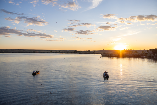 Boats on a calm river at sunrise near Montana fields and trees