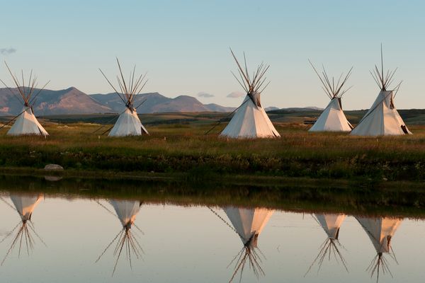 Tipis reflected in a calm pond with mountain views in Montana at dusk