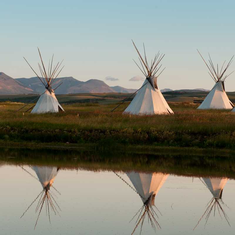 Tipis reflected in a calm pond with mountain views in Montana at dusk