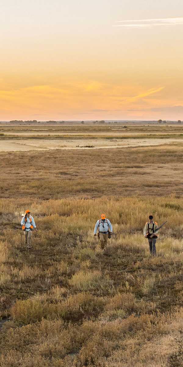 People walking on a prairie trail at sunset near a road and distant hills in Montana
