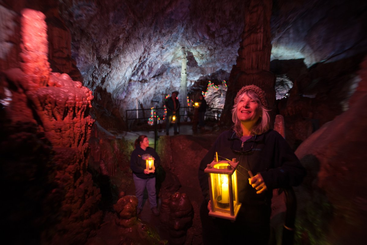 Visitors holding lanterns inside a dimly lit cave with warm lights along a path