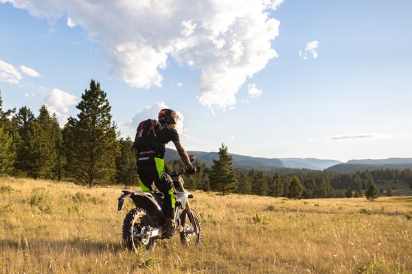 Person rides an all-terrain bike on a Montana meadow with forested hills in the distance under a partly cloudy sky