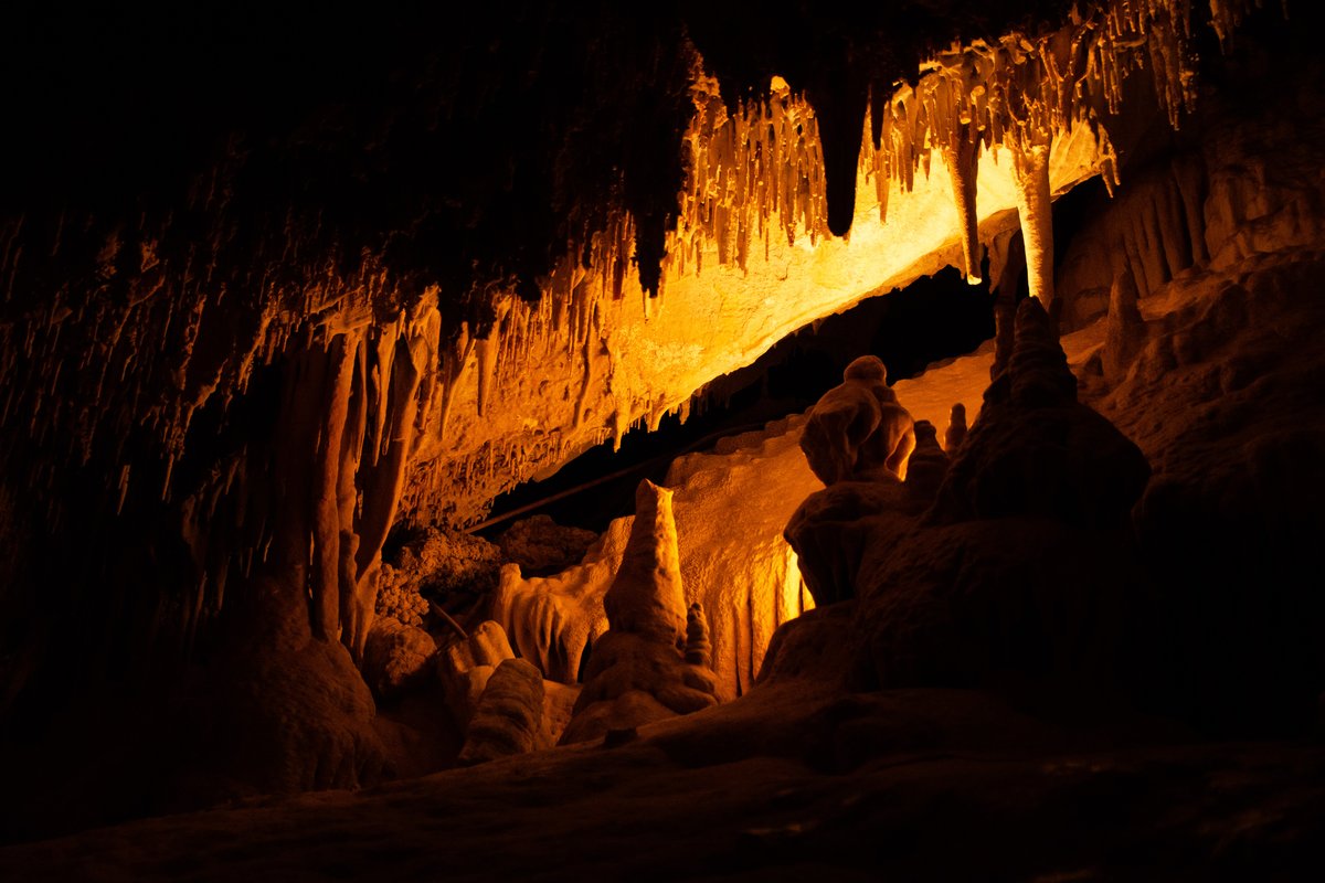 Candlelit interior of a Montana limestone cave with illuminated stalactites and stalagmites along the walkway
